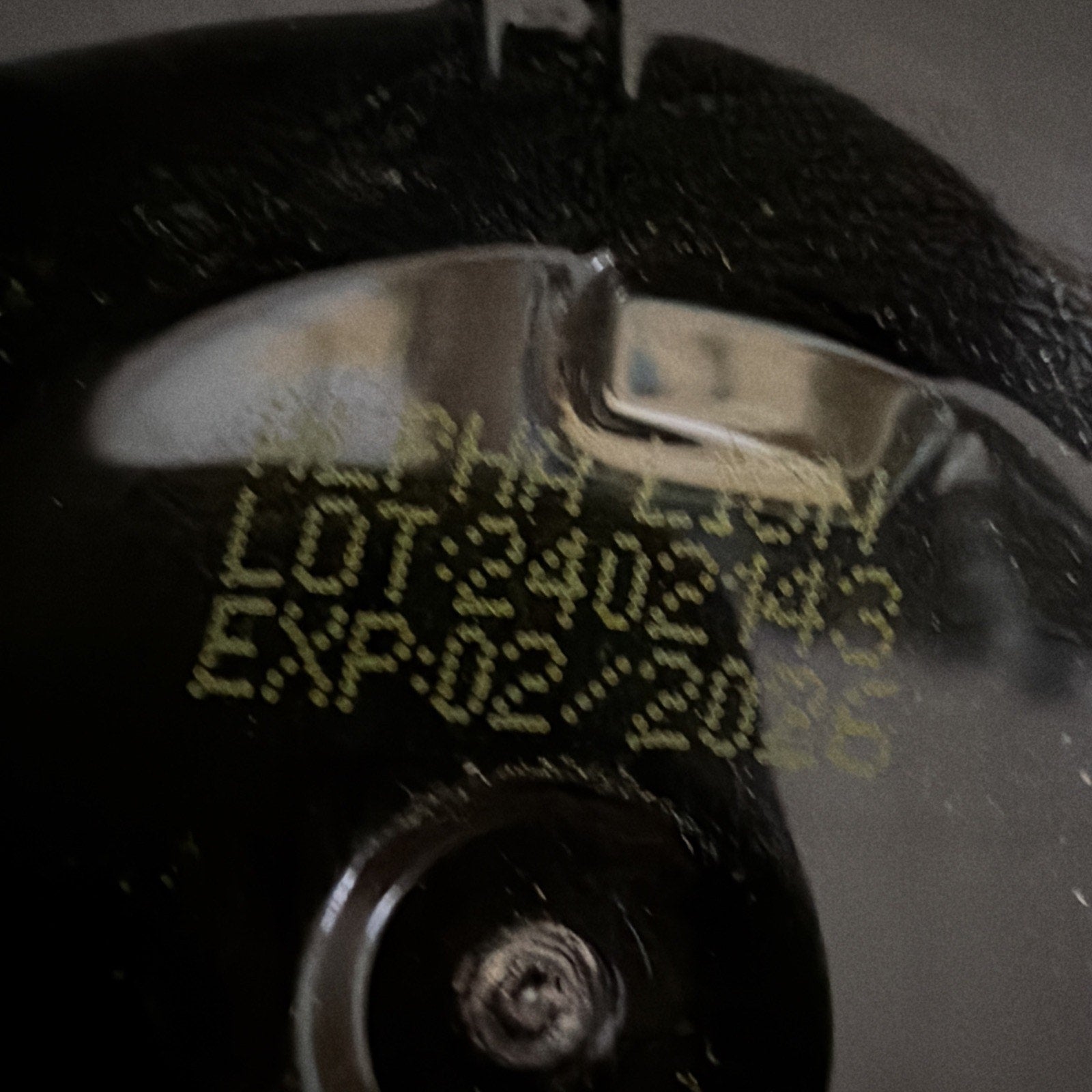 Close-up of a black textured surface with yellow printed lot number "3402143" and expiration date "02/2026" on a metallic reflective area.