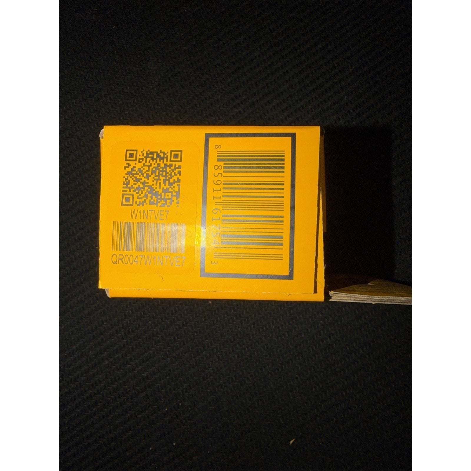 Yellow product box showing two barcode labels including a QR code and a standard barcode on a textured black surface.