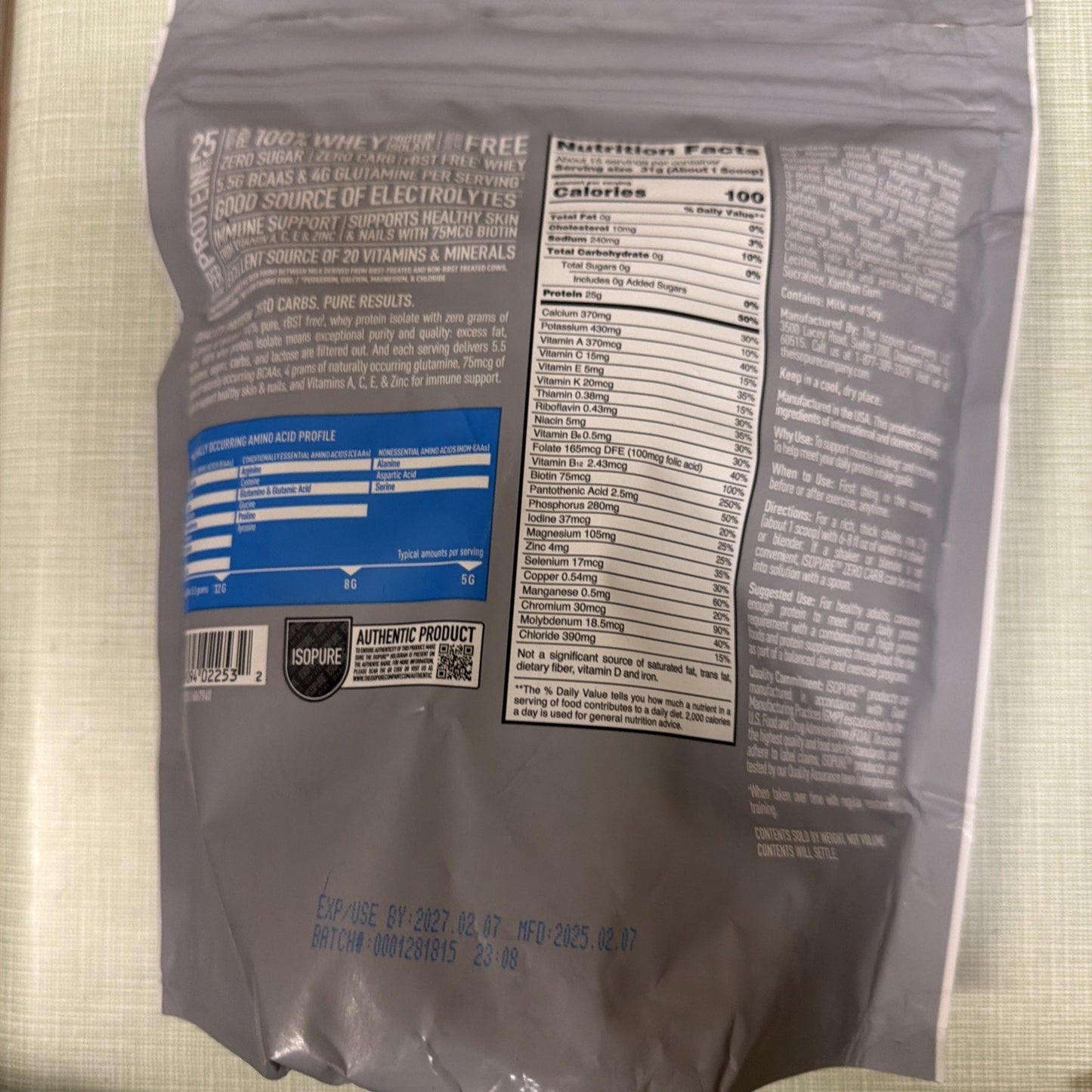 Back of a gray supplement package displaying detailed nutrition facts including calories and vitamins, amino acid profile chart, ingredient list, usage instructions, allergen warnings, barcode, and expiration and batch codes in blue ink.