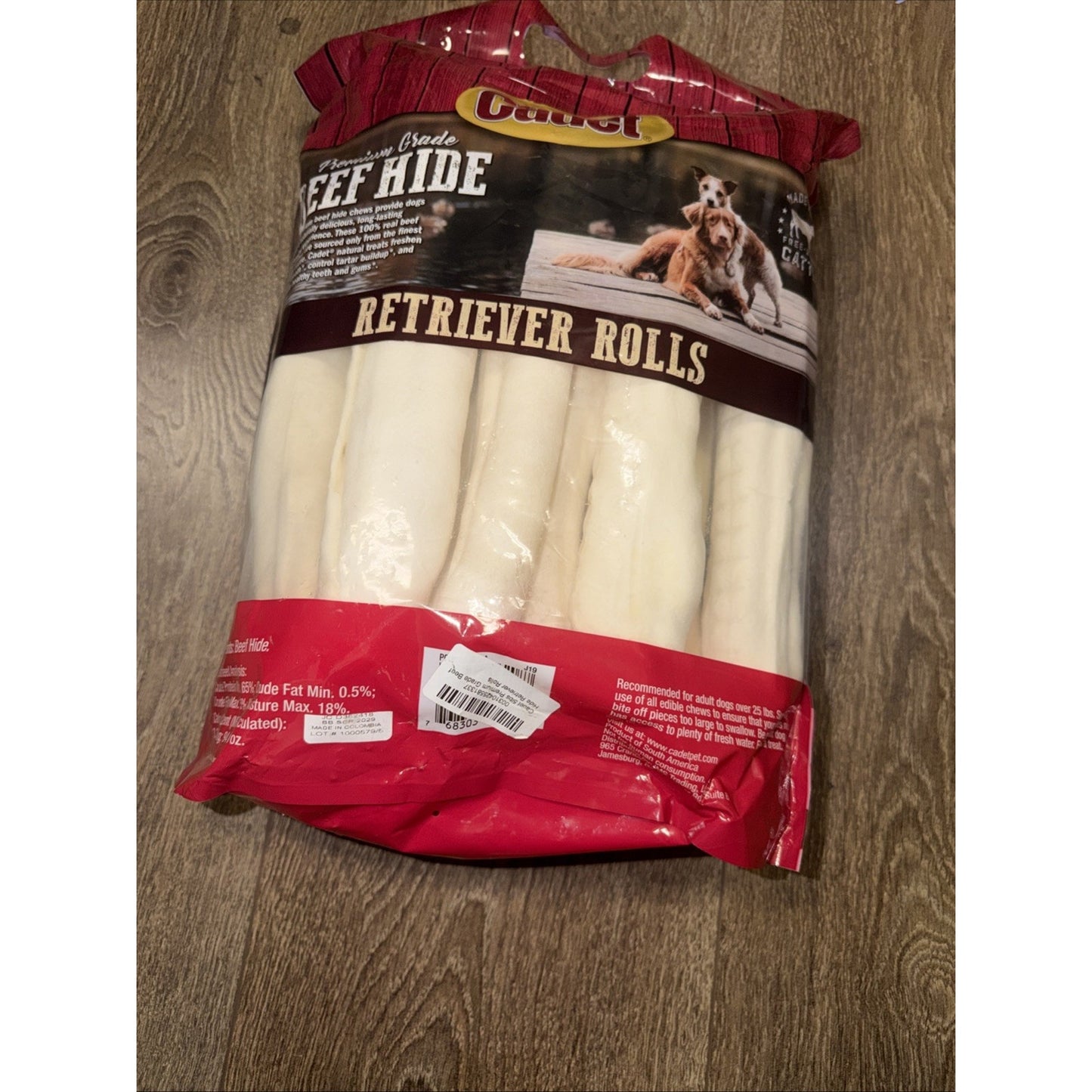 Clear plastic bag containing several white beef hide dog chews shaped as rolls, with a red and brown label featuring two retriever dogs and product branding on a wooden floor.
