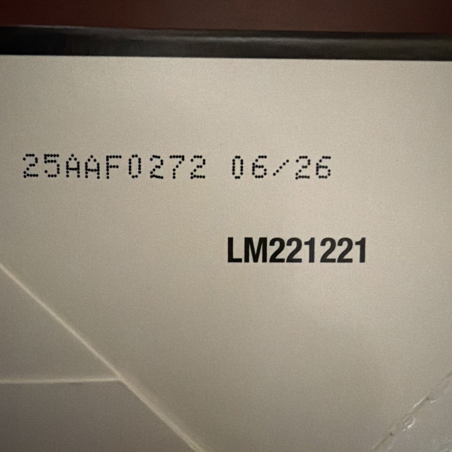 Close-up of a white surface showing printed code "25AAF0272 06/26" and bold text "LM221221" on a slightly textured background.