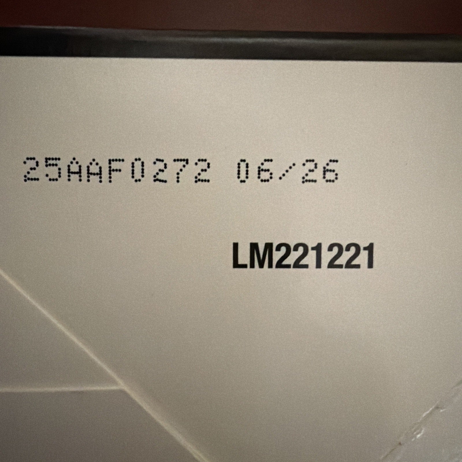 Close-up of a white surface showing printed code "25AAF0272 06/26" and bold text "LM221221" on a slightly textured background.