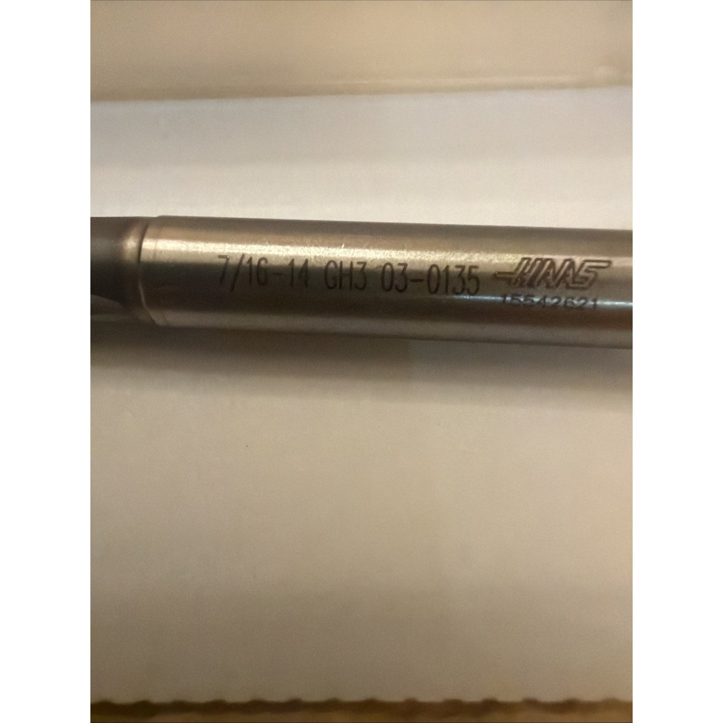 Close-up of a cylindrical metal tool with engraved text including size and product codes, resting on a white surface under soft lighting.