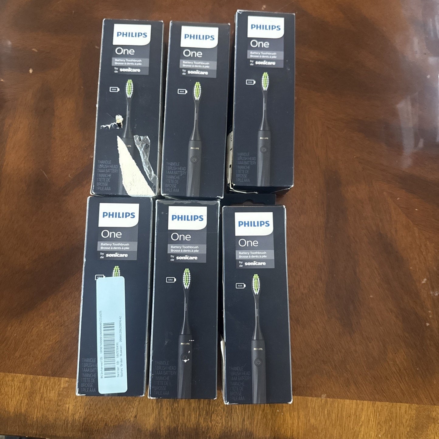 Six boxed Philips One Battery Toothbrushes by Sonicare model HY1100/54 displayed on wooden surface