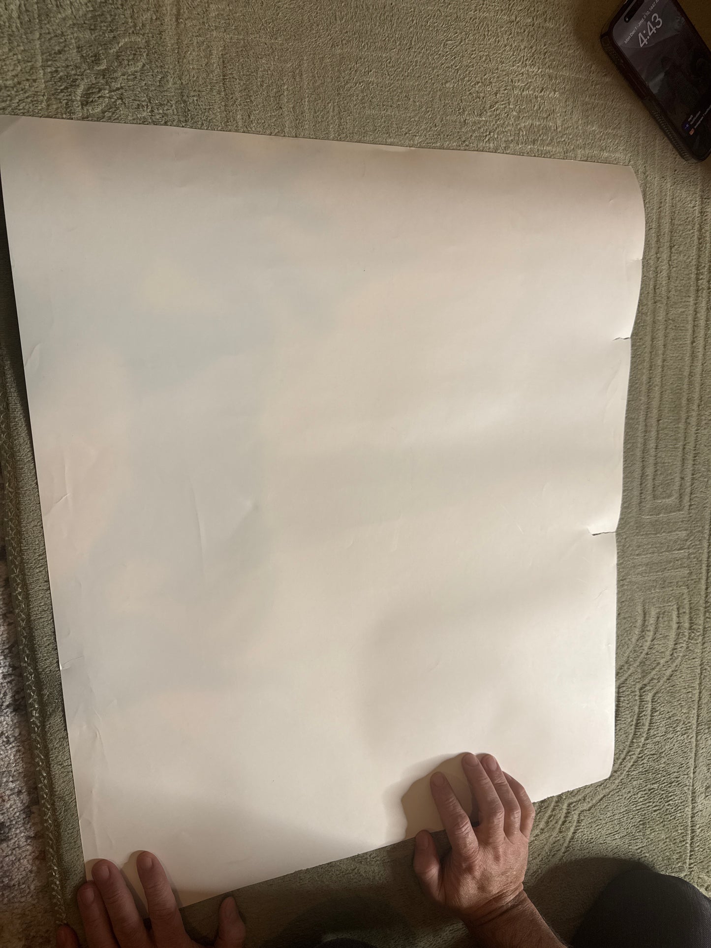 Blank white 20x24 photo paper held on carpeted floor with hands visible and phone nearby