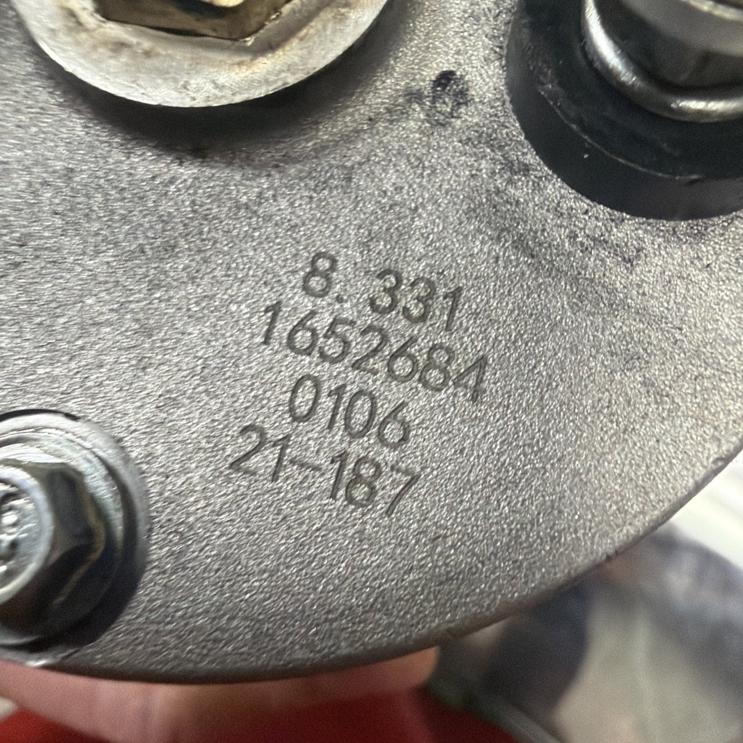 Close-up of a metallic component with engraved numbers "8-331," "1652684," "0106," and "21-187," showing bolts and a textured surface in a mechanical setting.