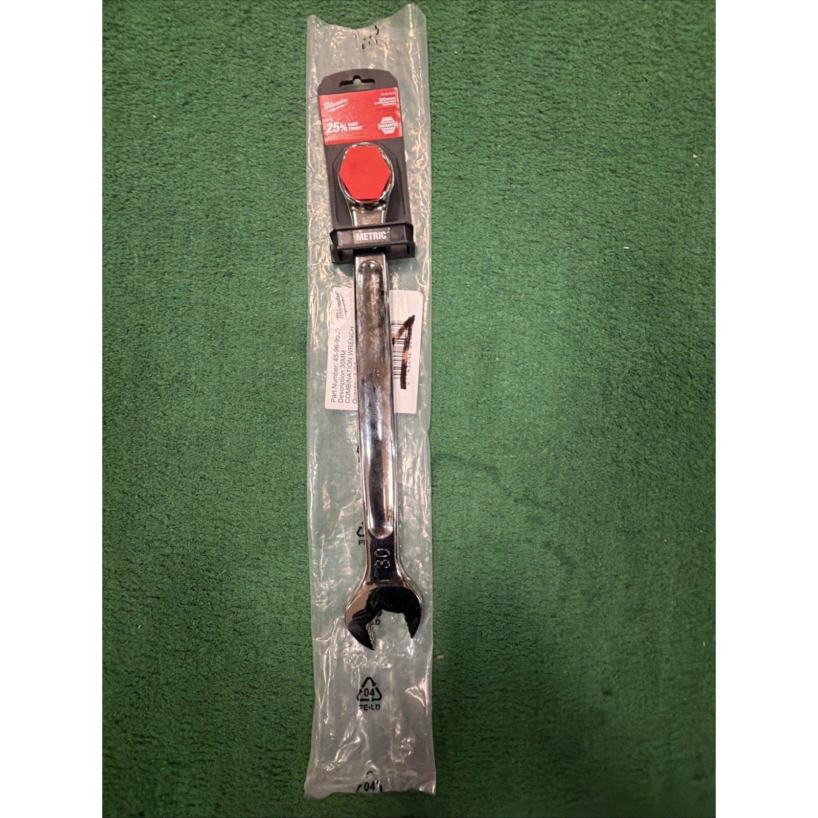 Metal open-end wrench with a polished finish, sealed in clear plastic packaging, resting on a green textured surface with a red label attached to the top.
