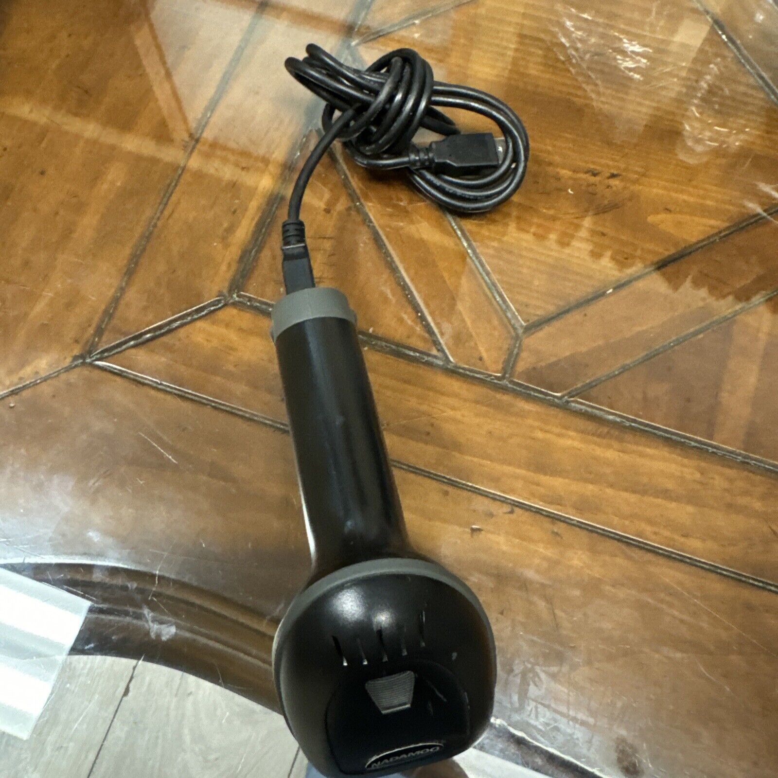 Black handheld barcode scanner with USB cable on glass and wooden patterned table surface