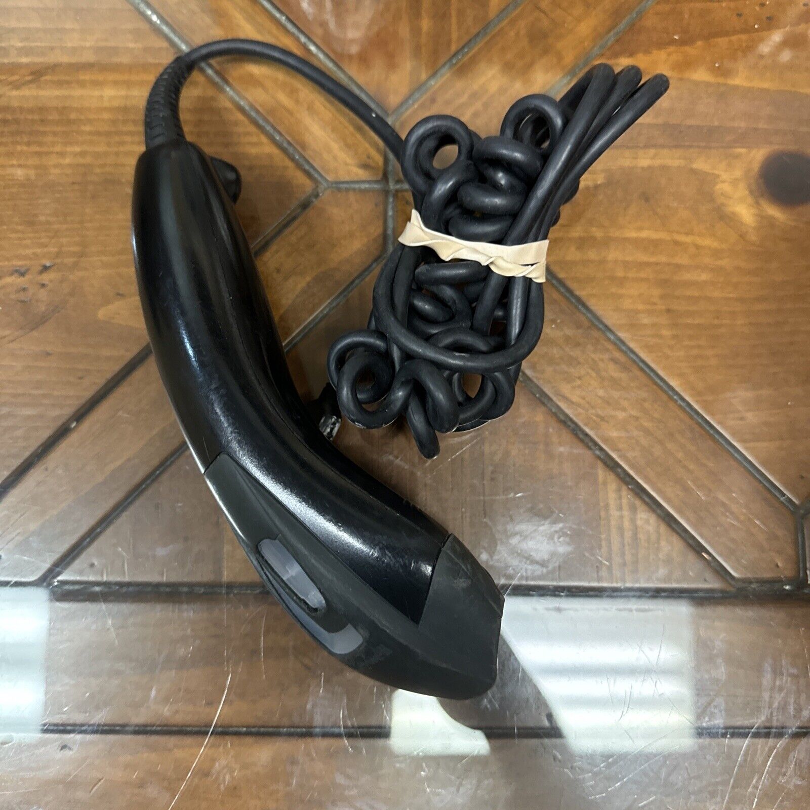 Used black Honeywell USB barcode scanner with coiled cable secured by rubber band on wooden surface