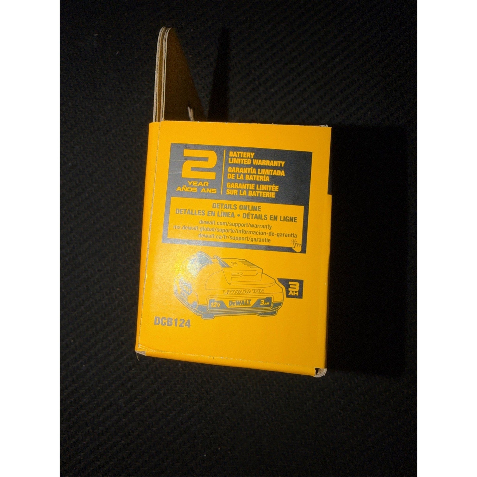Yellow product box showing a 2-year limited battery warranty label, warranty details in multiple languages, and a small graphic of a cordless power tool on a dark textured surface.