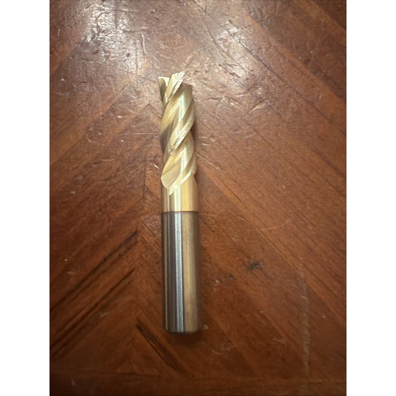 Single carbide end mill with gold-colored spiral cutting edges and smooth silver shank resting on a wooden surface.