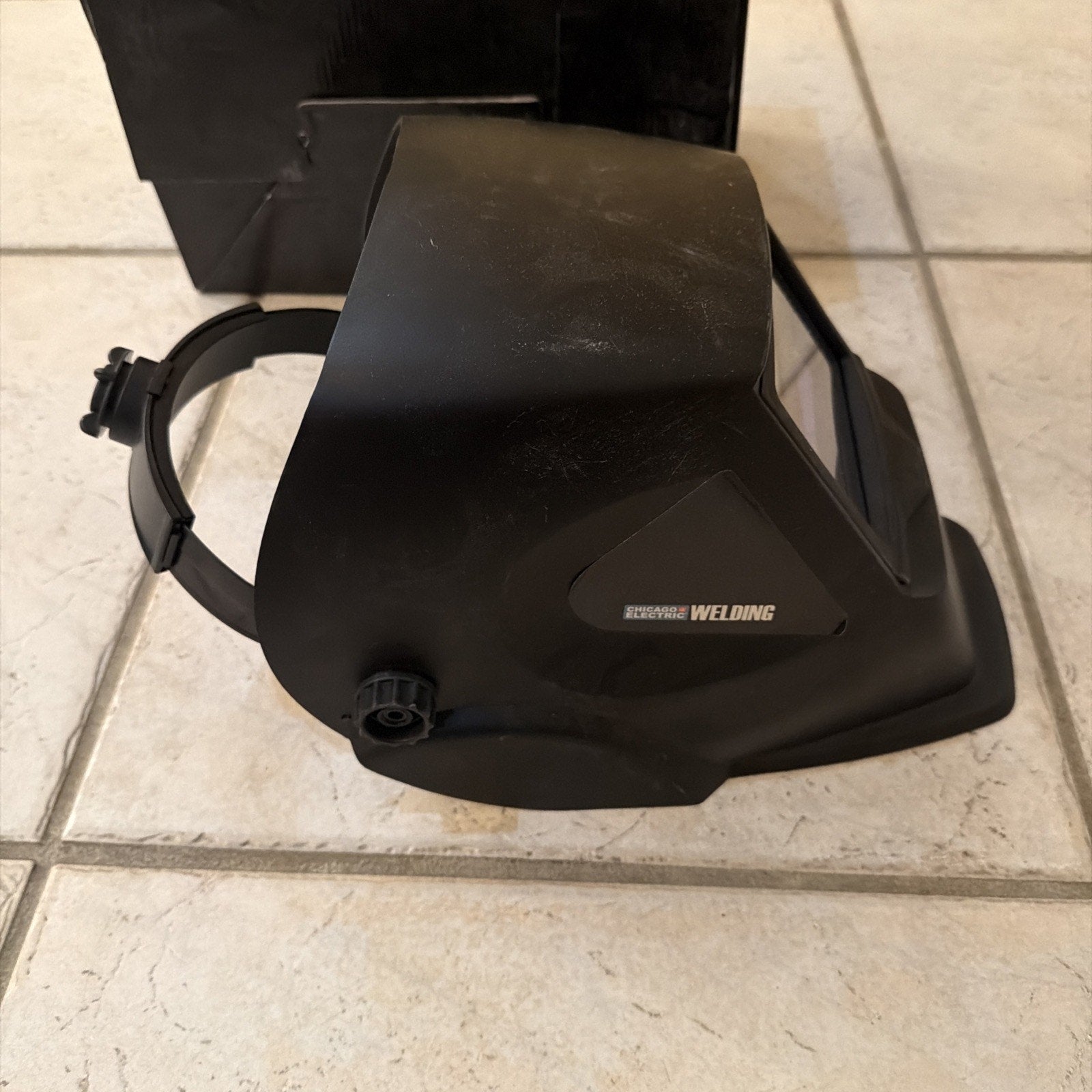 Chicago Electric black auto-darkening welding helmet with adjustable shade and durable plastic lens on tiled floor