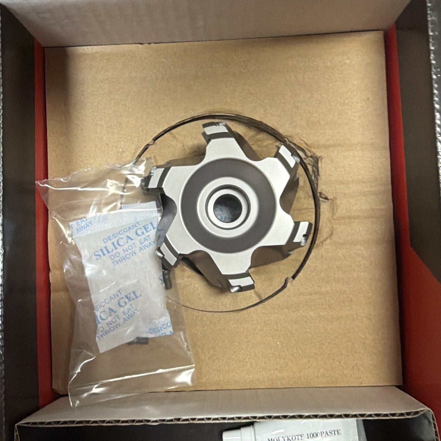 Six-toothed silver cutting tool with a central hole, packaged inside a cardboard box alongside a small sealed silica gel packet in a clear plastic bag.