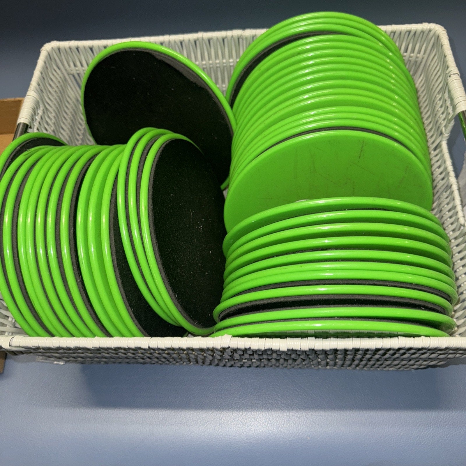 Set of 43 green exercise sliders with black tops stacked in white basket for Pilates abs yoga workouts