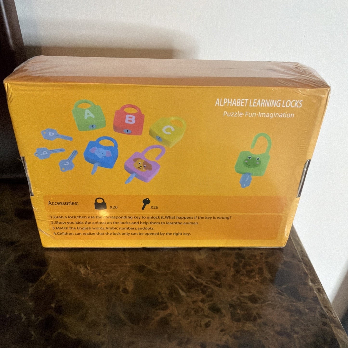 Yellow box packaging for a children’s educational toy set featuring colorful plastic locks shaped like animals and letters with matching keys to encourage learning and problem-solving skills.
