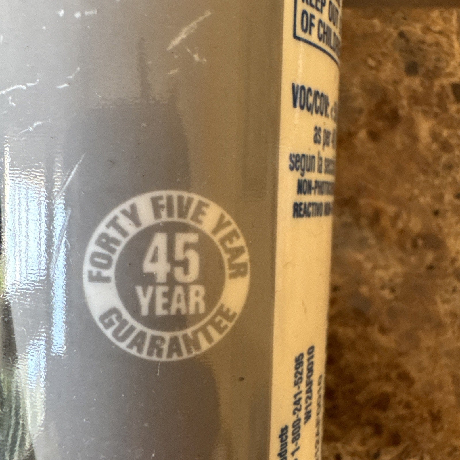 Close-up of a circular label on a grey surface stating a forty-five year guarantee with partial text of safety and chemical information on a beige label in the background.
