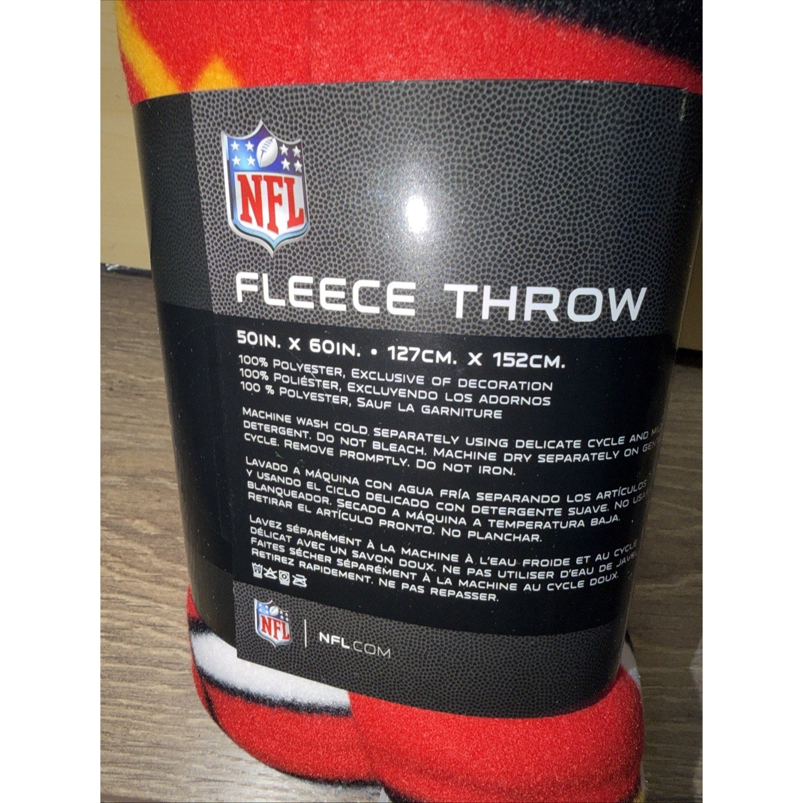 Black textured packaging label showing NFL logo and product information, including dimensions and care instructions for a red fleece throw blanket.