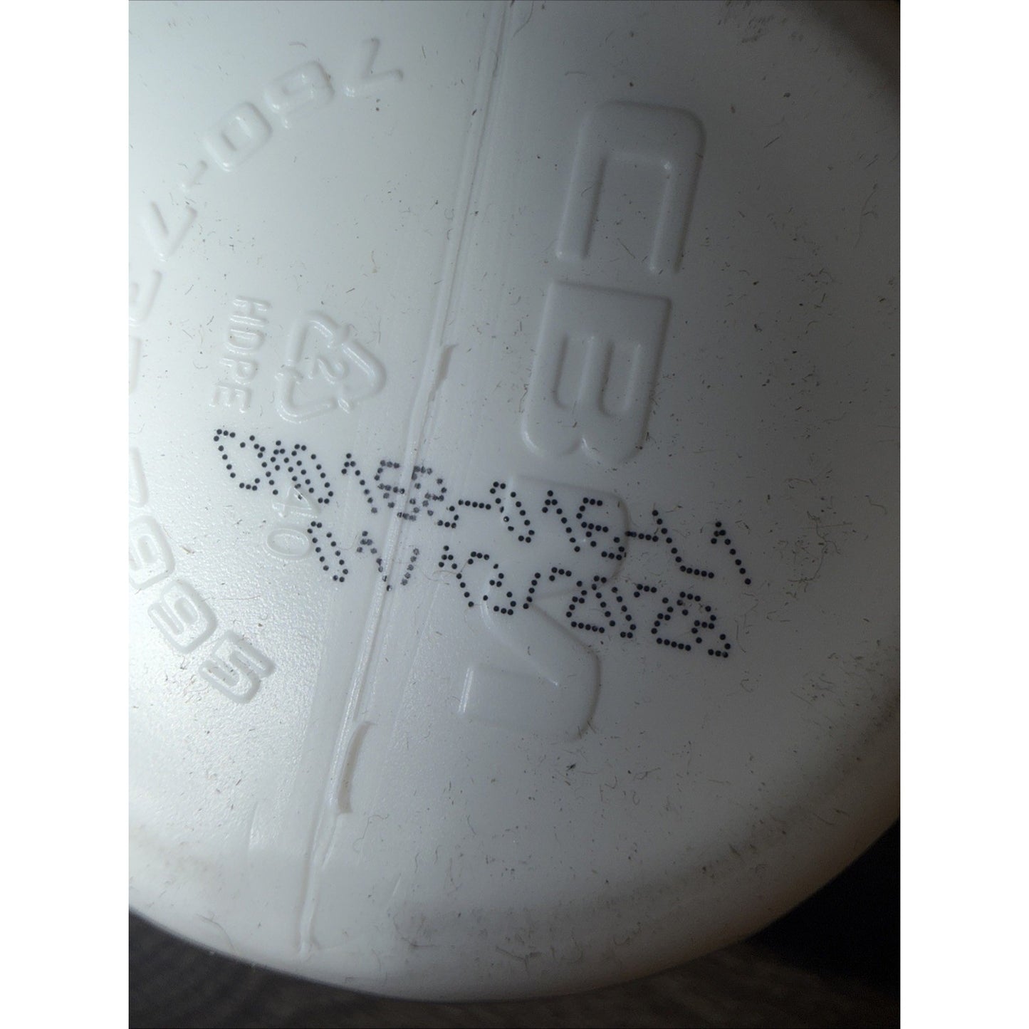 Close-up of a white plastic container lid with molded recycling symbols and embossed alphanumeric codes, featuring a printed date code in black ink.