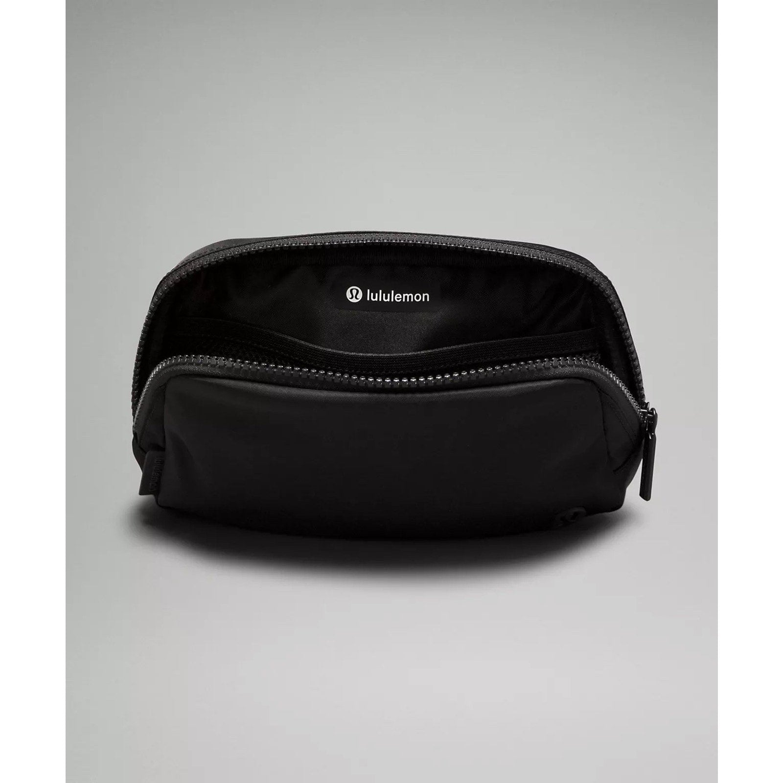 Open black zippered pouch with fabric lining and Lululemon logo visible inside, resting on a gray surface with soft lighting.