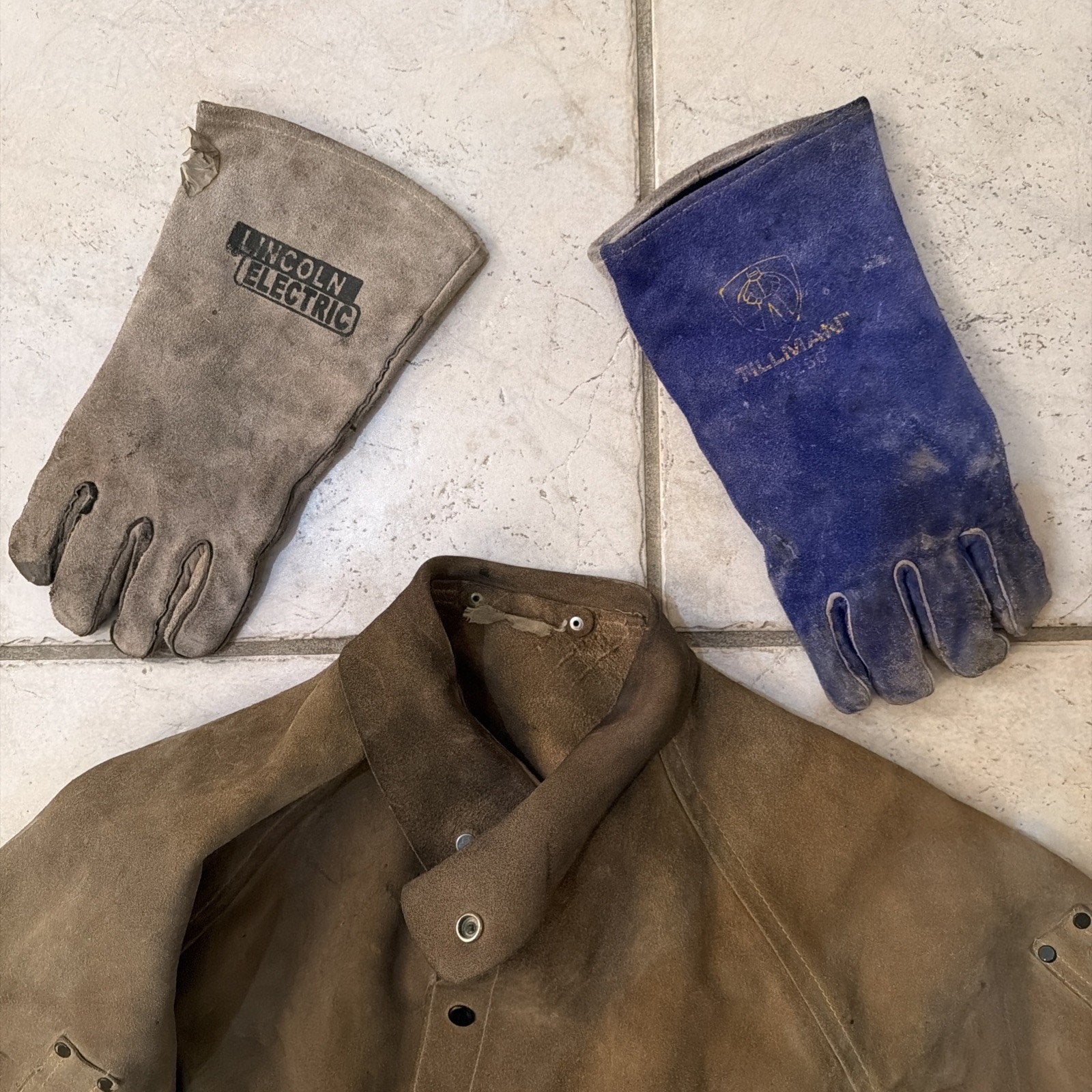 Worn leather welding jacket and two heavy-duty leather welding gloves branded Lincoln Electric and Millitant