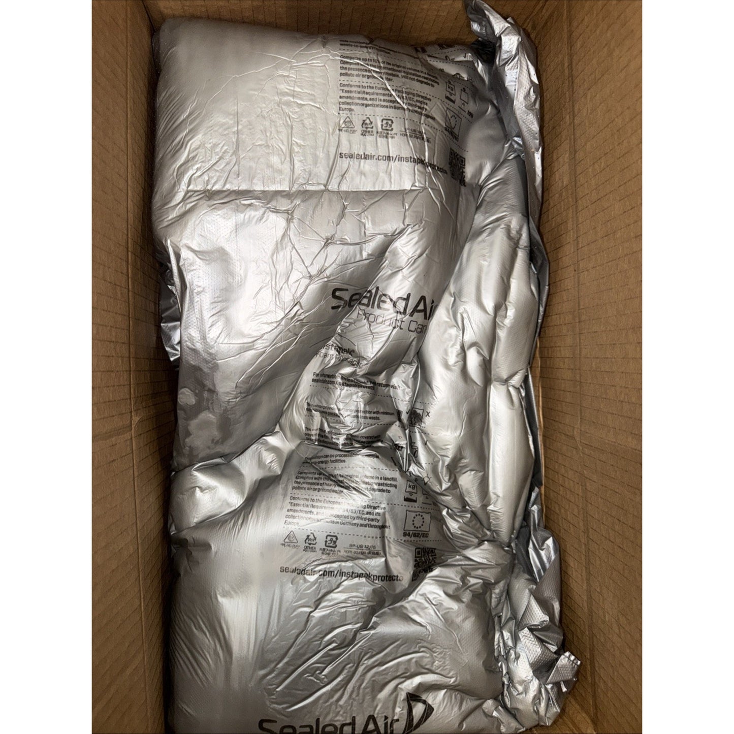 Brown cardboard box containing multiple inflated silver air cushioning packs labeled with the Sealed Air logo for protective packaging.