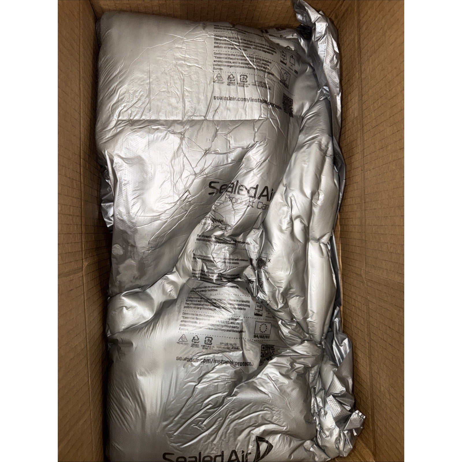 Brown cardboard box containing multiple inflated silver air cushioning packs labeled with the Sealed Air logo for protective packaging.