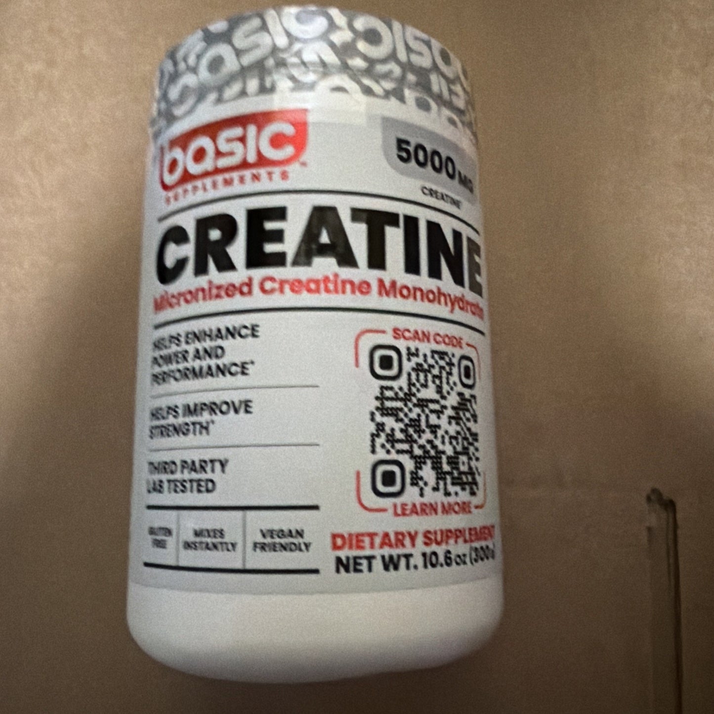 White plastic container of micronized creatine monohydrate supplement with red and black text highlighting benefits for strength and performance, featuring a QR code on the label.