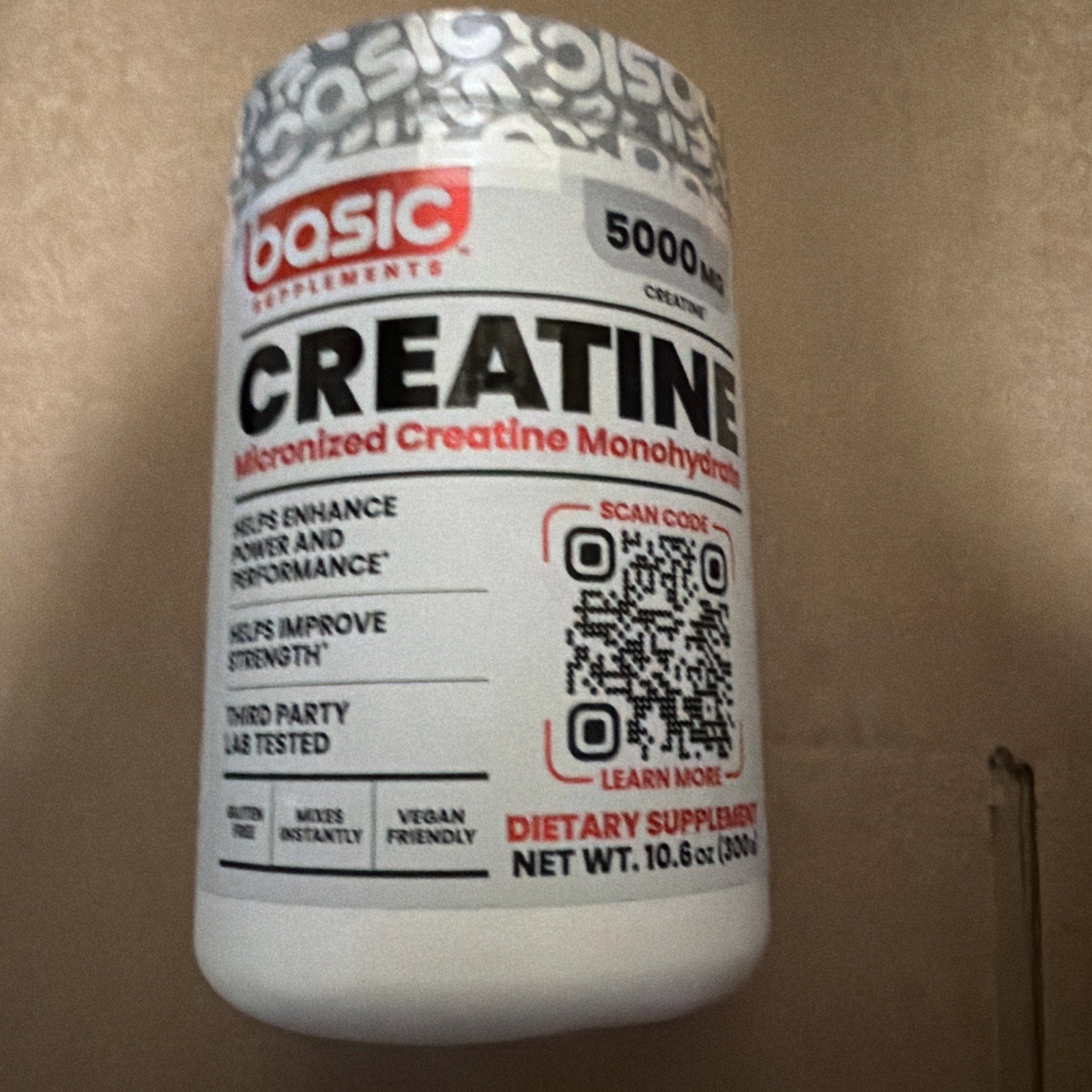 White plastic container of micronized creatine monohydrate supplement with red and black text highlighting benefits for strength and performance, featuring a QR code on the label.