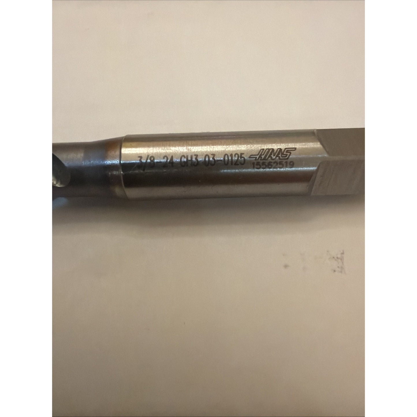 Close-up of a cylindrical metal tool with engraved size and product numbers alongside a Haas logo, resting horizontally on a plain light surface.