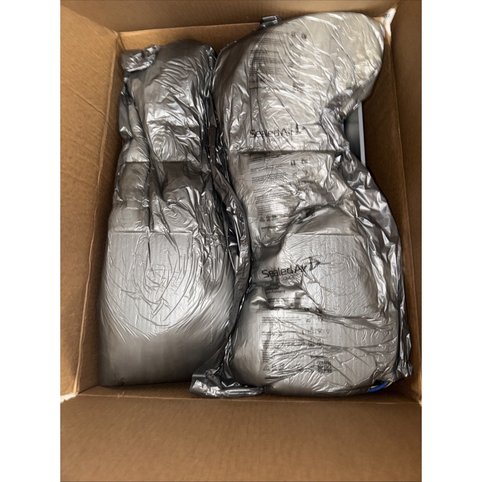 Two large silver vacuum-sealed bags containing unidentified items placed inside an open brown cardboard box.
