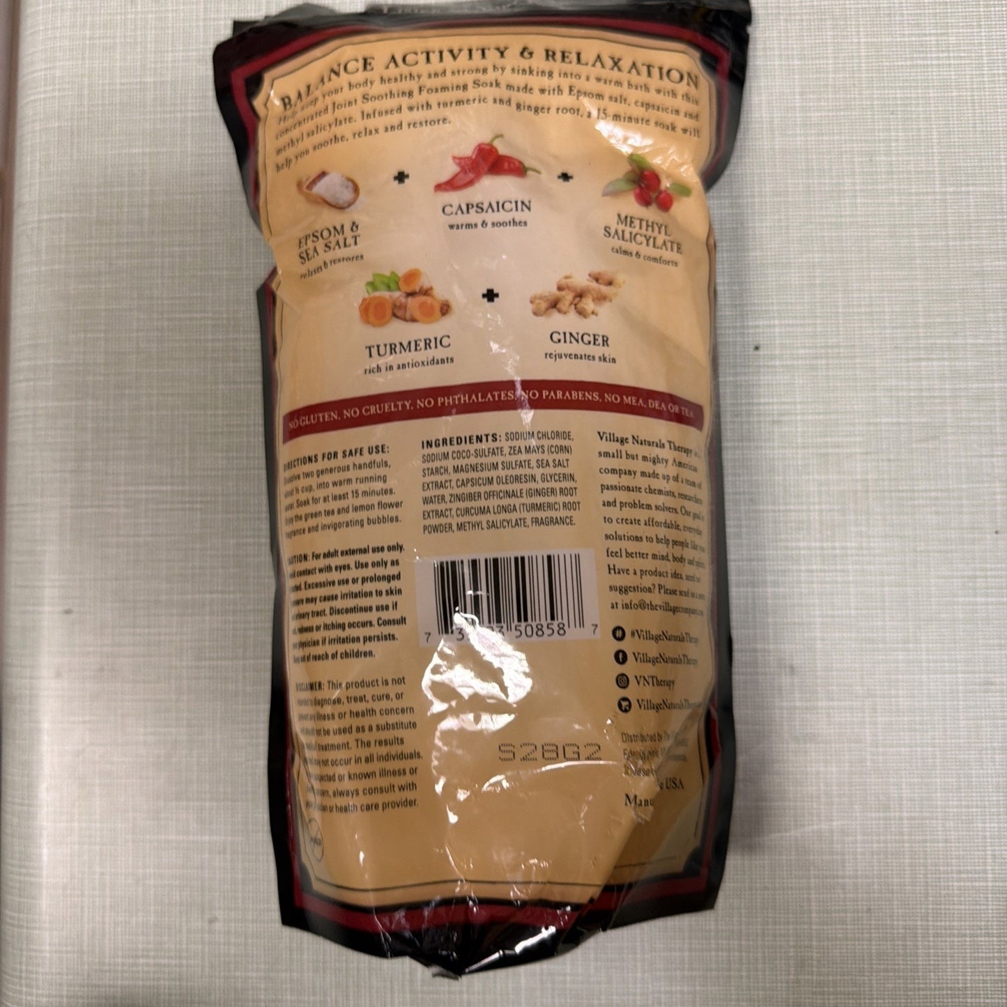 Back view of a brown and black pouch featuring detailed ingredient list and product benefits highlighting Epsom and sea salt, capsicin, methyl salicylate, turmeric, and ginger for balance, activity, and relaxation.