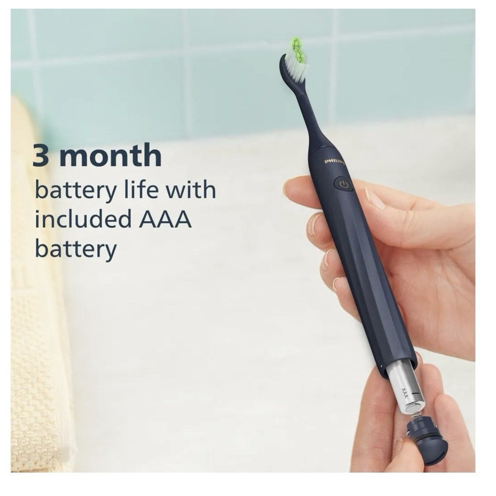 Hand holding black Philips Sonicare One toothbrush showing AAA battery insertion and battery life text on wall
