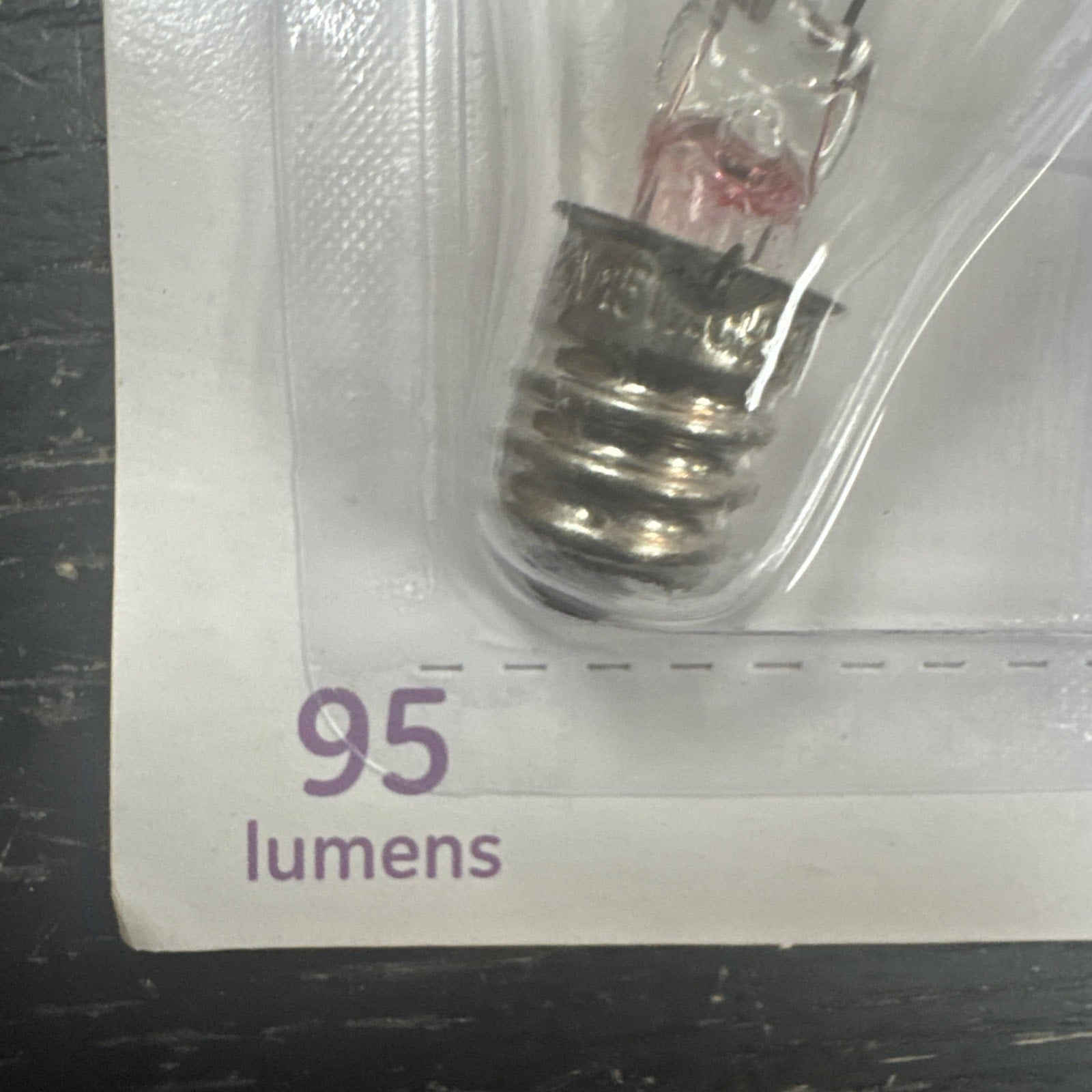 Close-up of GE crystal clear soft white 15 watt light bulb showing base and 95 lumens label on packaging