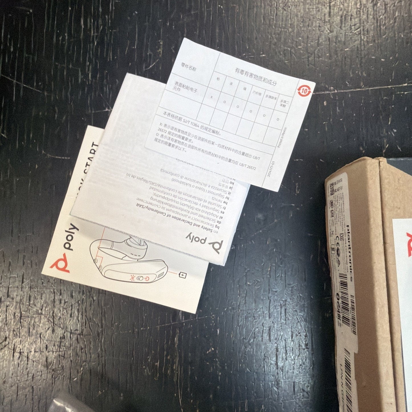 Instruction manuals and a small paper card with charts and text in a foreign language, placed on a dark wooden surface next to a partially visible cardboard box.