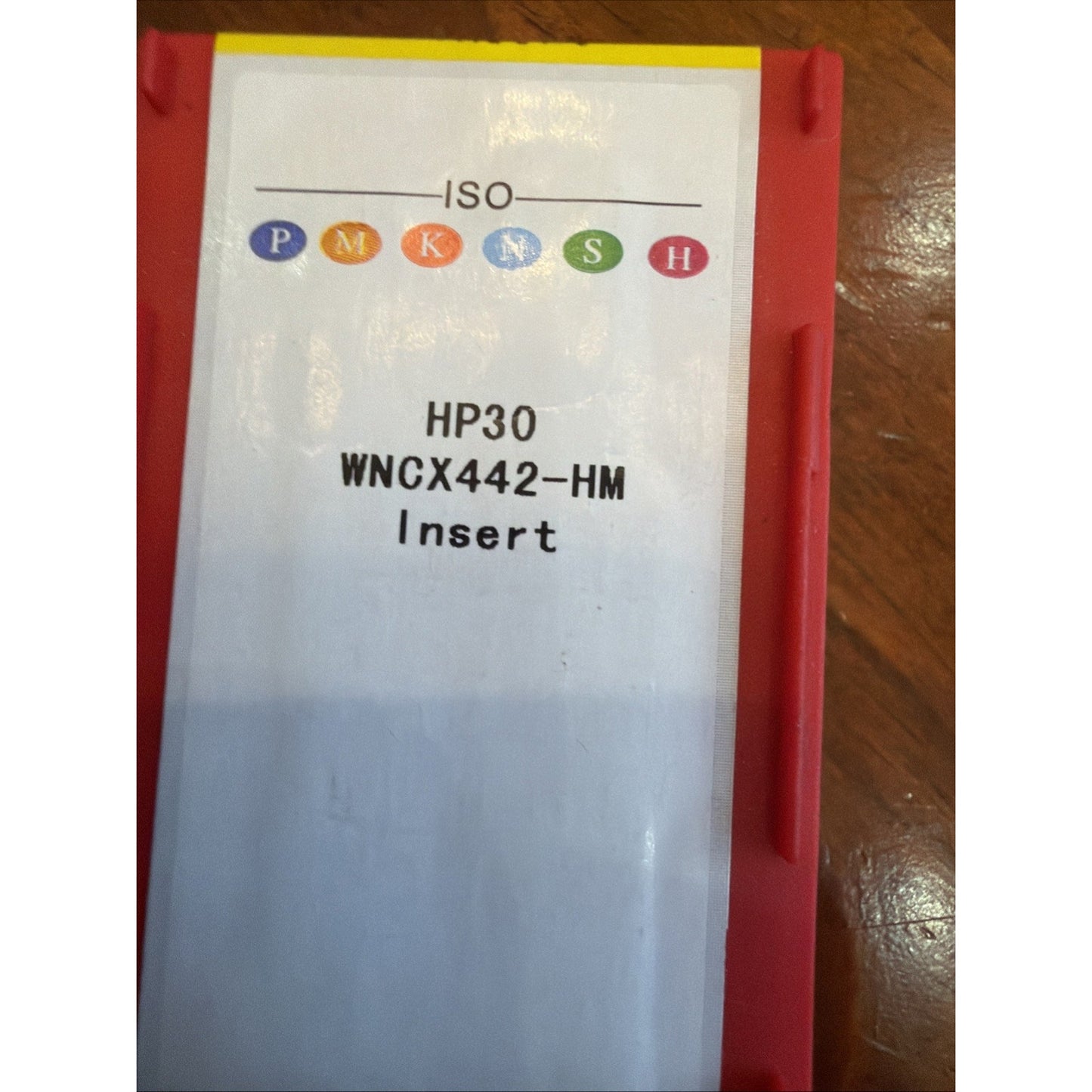 Red plastic case with a white label showing colored ISO codes and text reading "HP30 WNCX442-HM Insert" on a wooden surface.