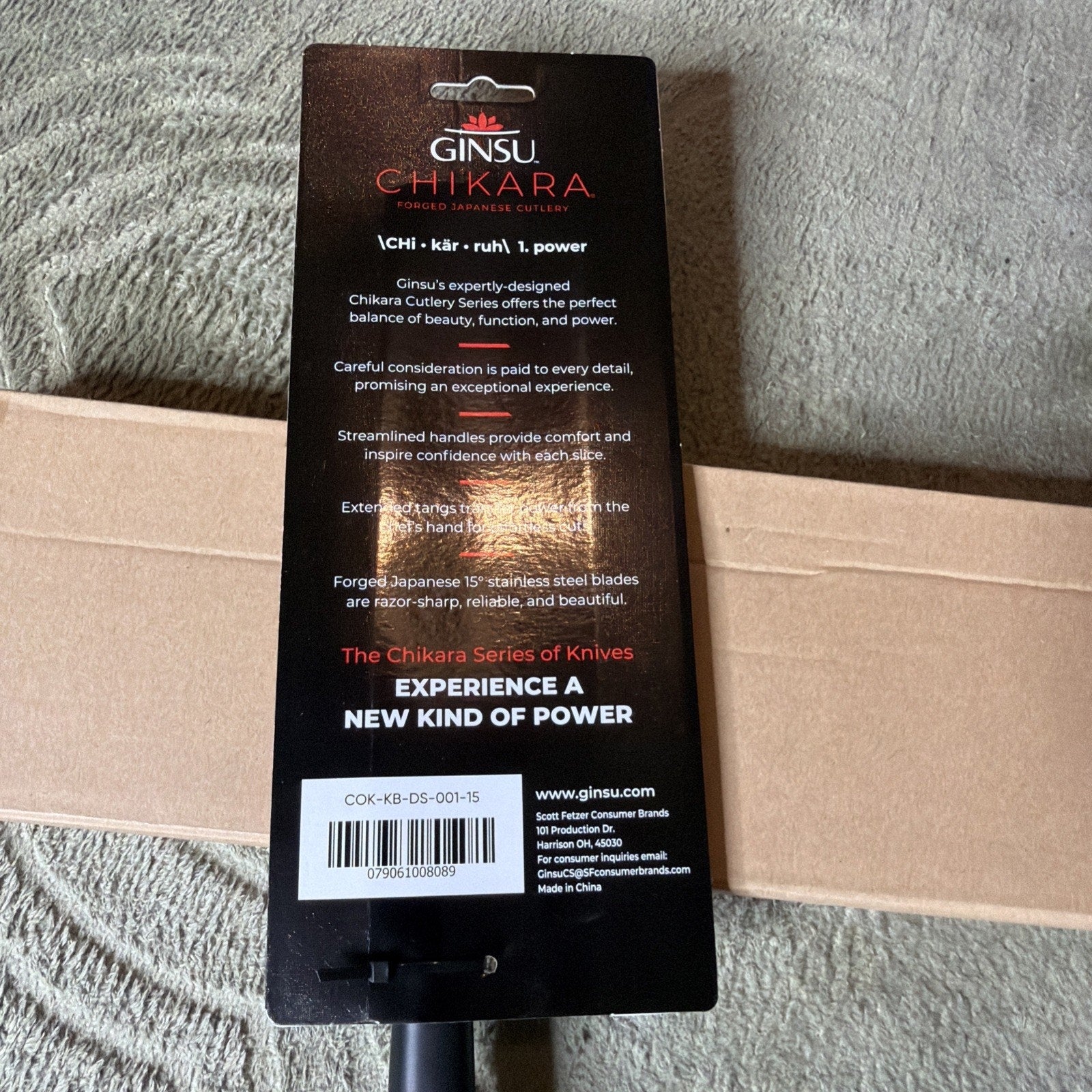 Back view of Ginsu Chikara knife packaging featuring product description about design, comfort, forged Japanese stainless steel blades, and a barcode label with company contact information.