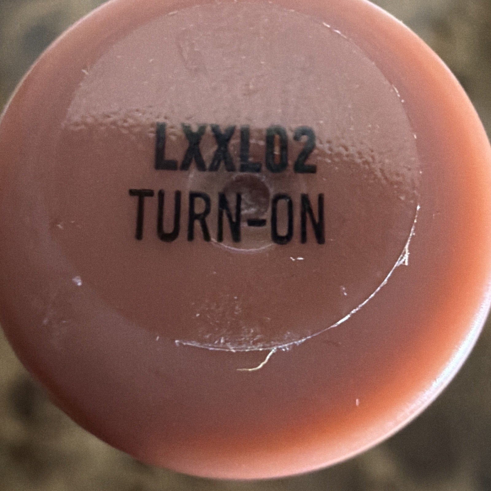 Close-up view of a circular pink plastic object with a transparent sticker displaying the black printed text "LXXL02 TURN-ON" on its surface.