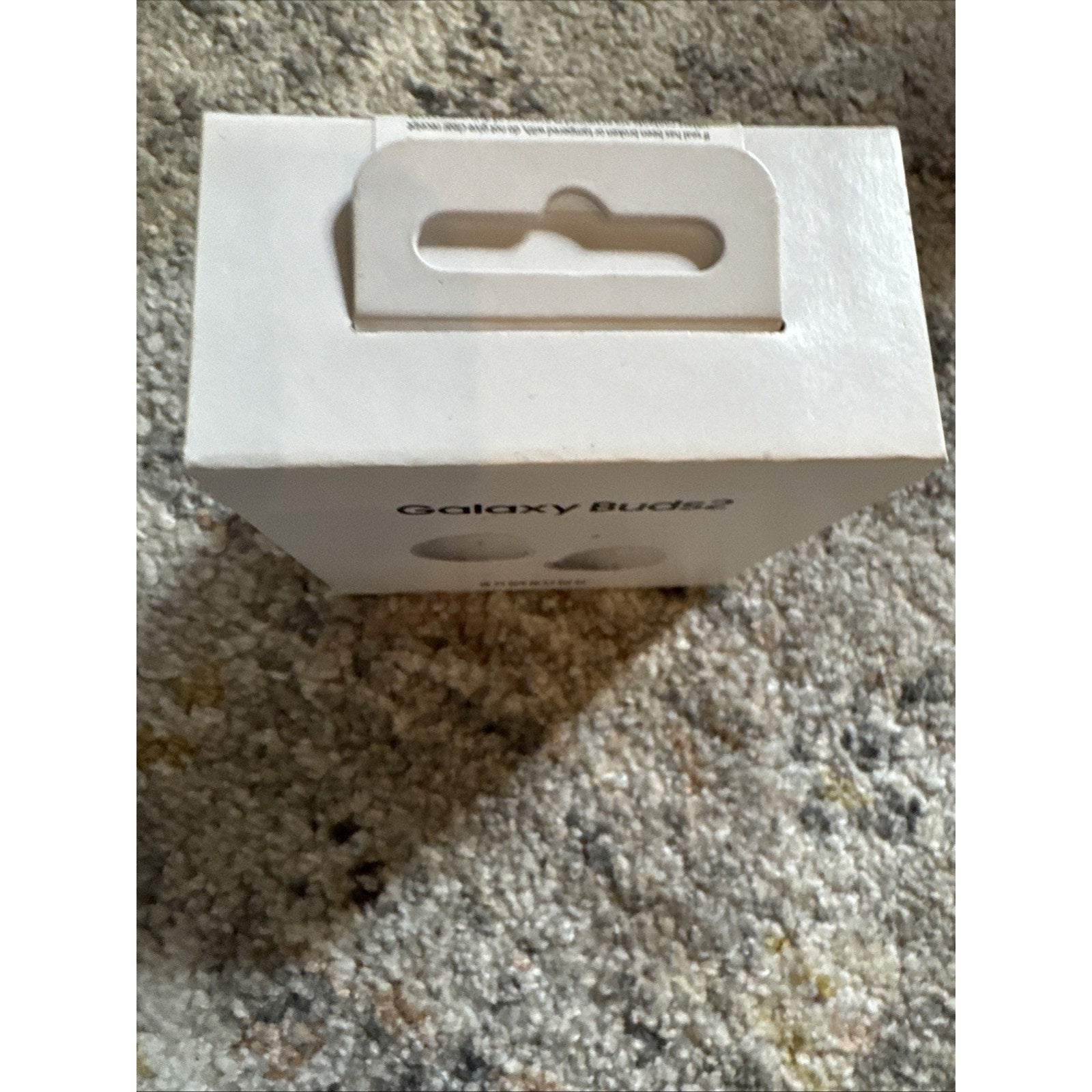 Packaging box for brand new Samsung Galaxy Buds2 wireless earbuds in white color placed on textured carpet background