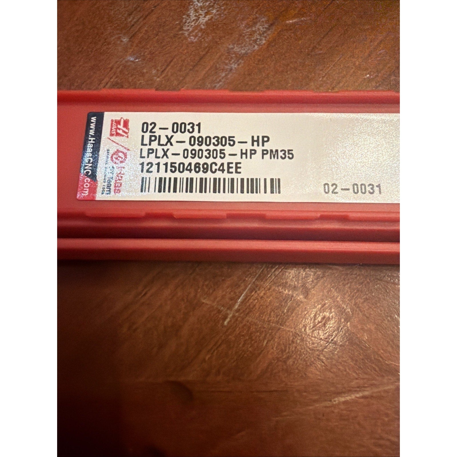 Red rectangular plastic case with a white label displaying product codes "LPLX-090305-HP" and "LPLX-090305-HP PM35," a barcode, and numeric identifier, resting on a wooden surface.