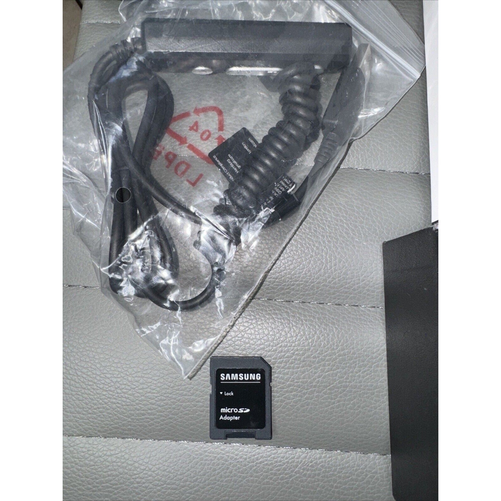 Samsung microSD card adapter with various coiled and straight camera cables in plastic bag on gray surface