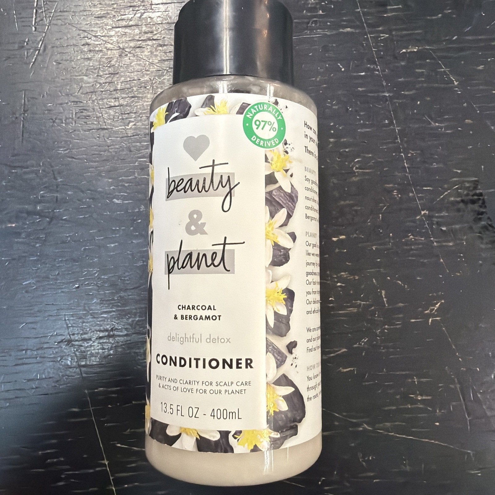 Plastic bottle of Beauty & Planet conditioner with charcoal and bergamot, featuring floral and charcoal graphics on the label and a black flip-top cap.