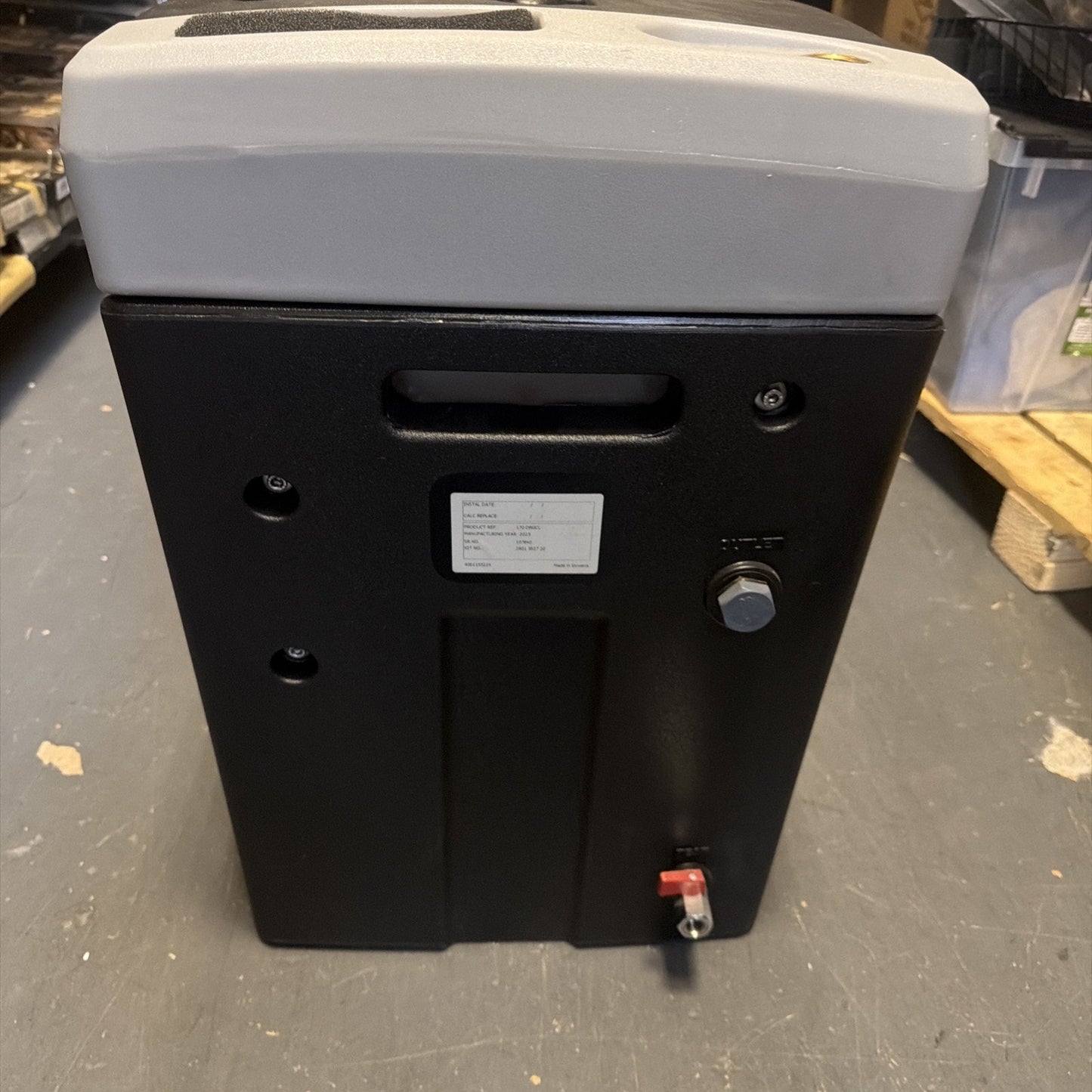 Black and gray rectangular industrial device with a small white label on the front, a handle slot near the top, two visible connectors on the right side, and placed on a gray concrete floor.