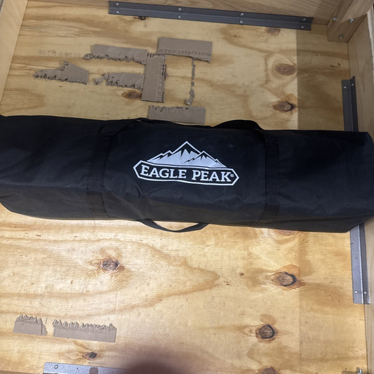 Eagle Peak 4x4 pop-up canopy tent frame folded inside black carry bag with logo on wooden surface