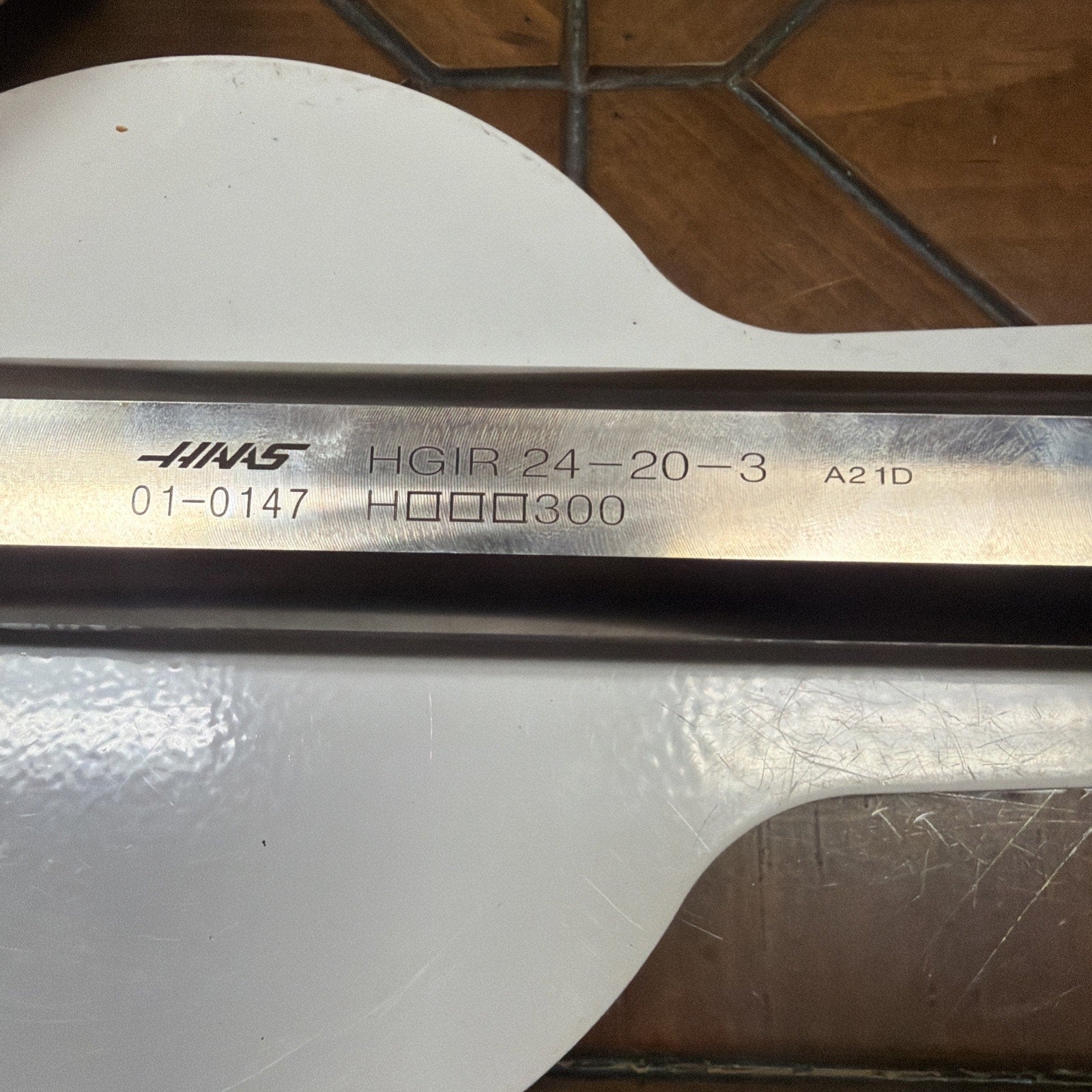 Close-up of a metallic tool shaft engraved with the brand name, product code "HGIR 24-20-3," serial number, and other alphanumeric markings, resting on a white surface with a wooden background.