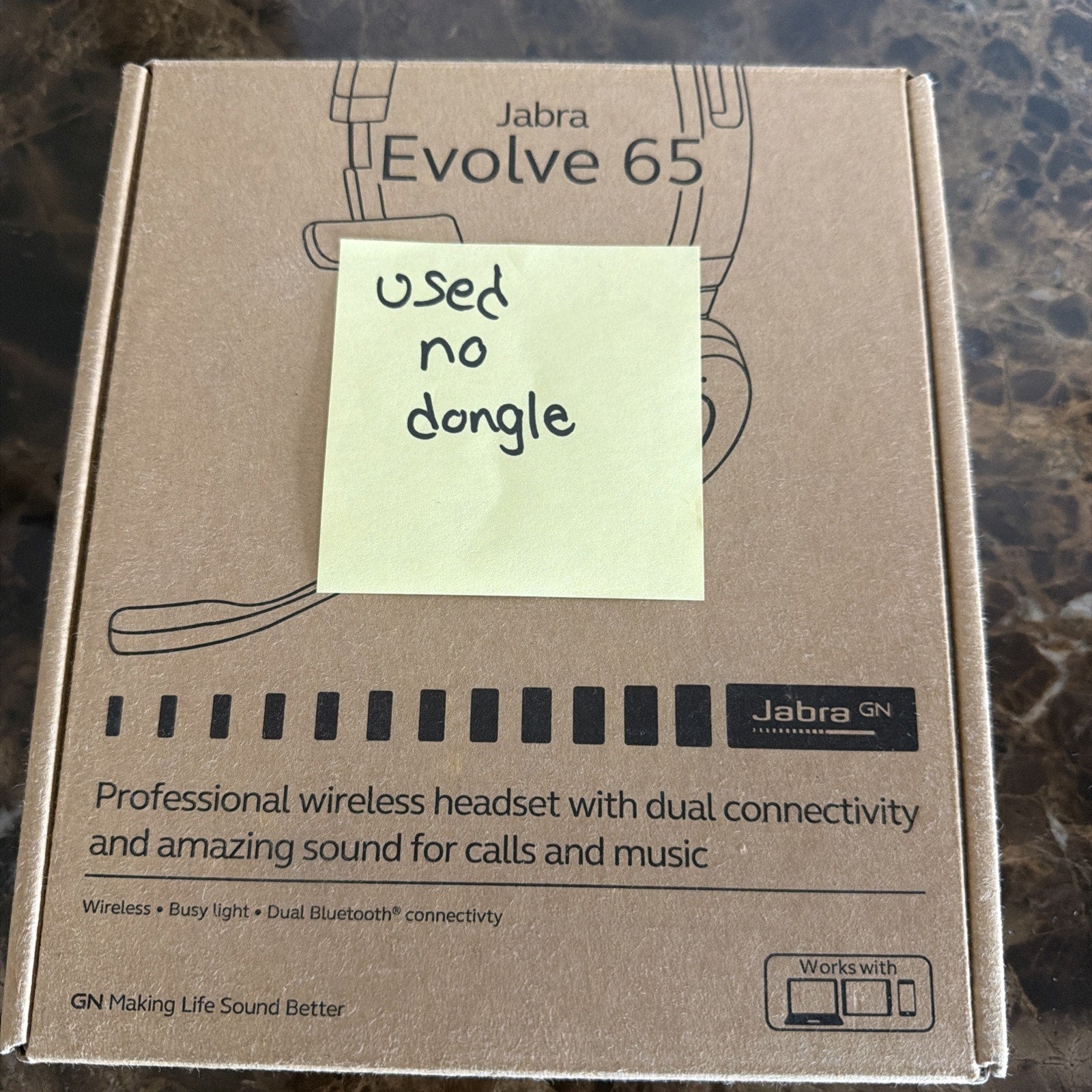 Brown cardboard box packaging for a Jabra Evolve 65 wireless headset displaying product features, with a yellow sticky note reading "used no dongle" placed on top.