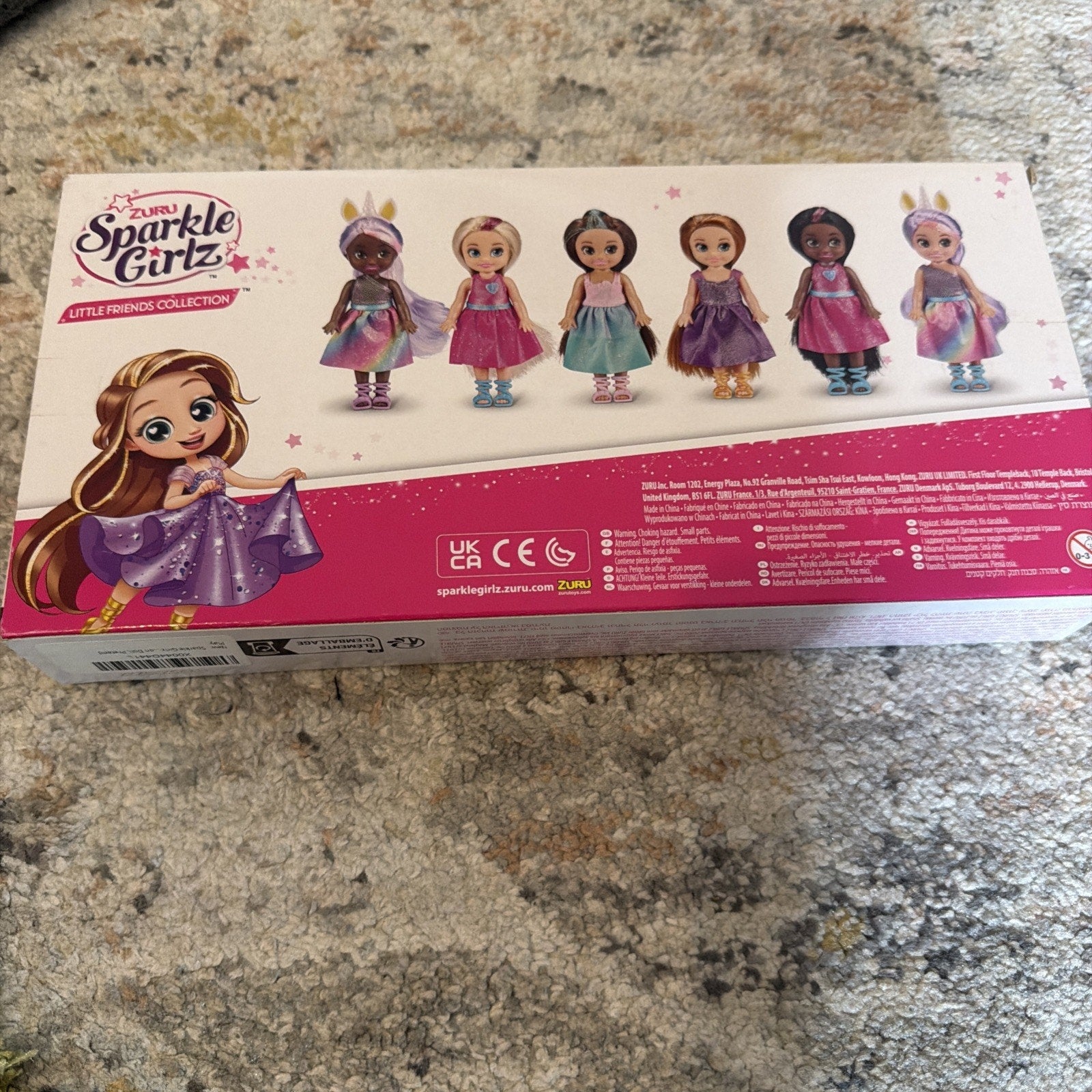 Toy packaging box displaying six small dolls in colorful dresses with wings, crowns, and boots, illustrated with a cartoon girl wearing a sparkling purple dress on the side.