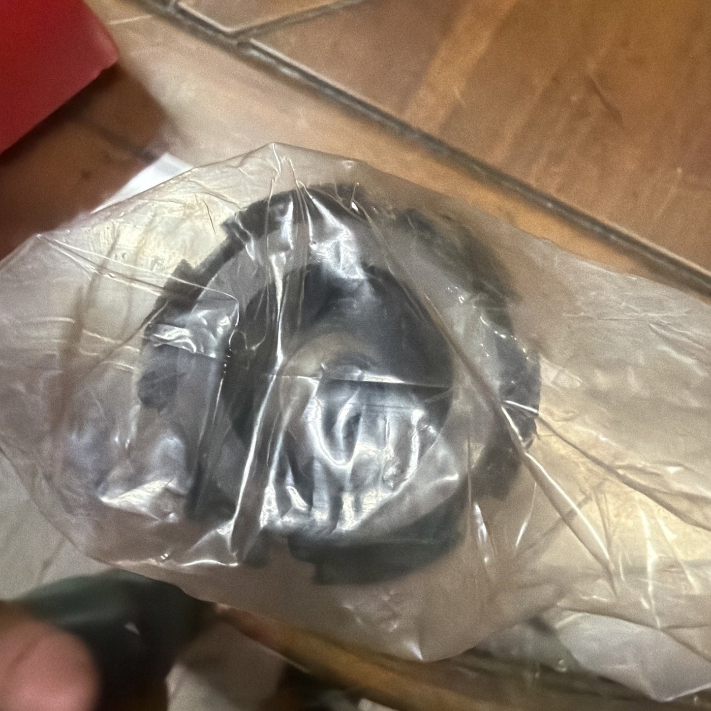 Black coiled cable or hose partially wrapped in a transparent plastic bag, resting on a wooden surface with visible grain and nearby objects slightly out of focus.