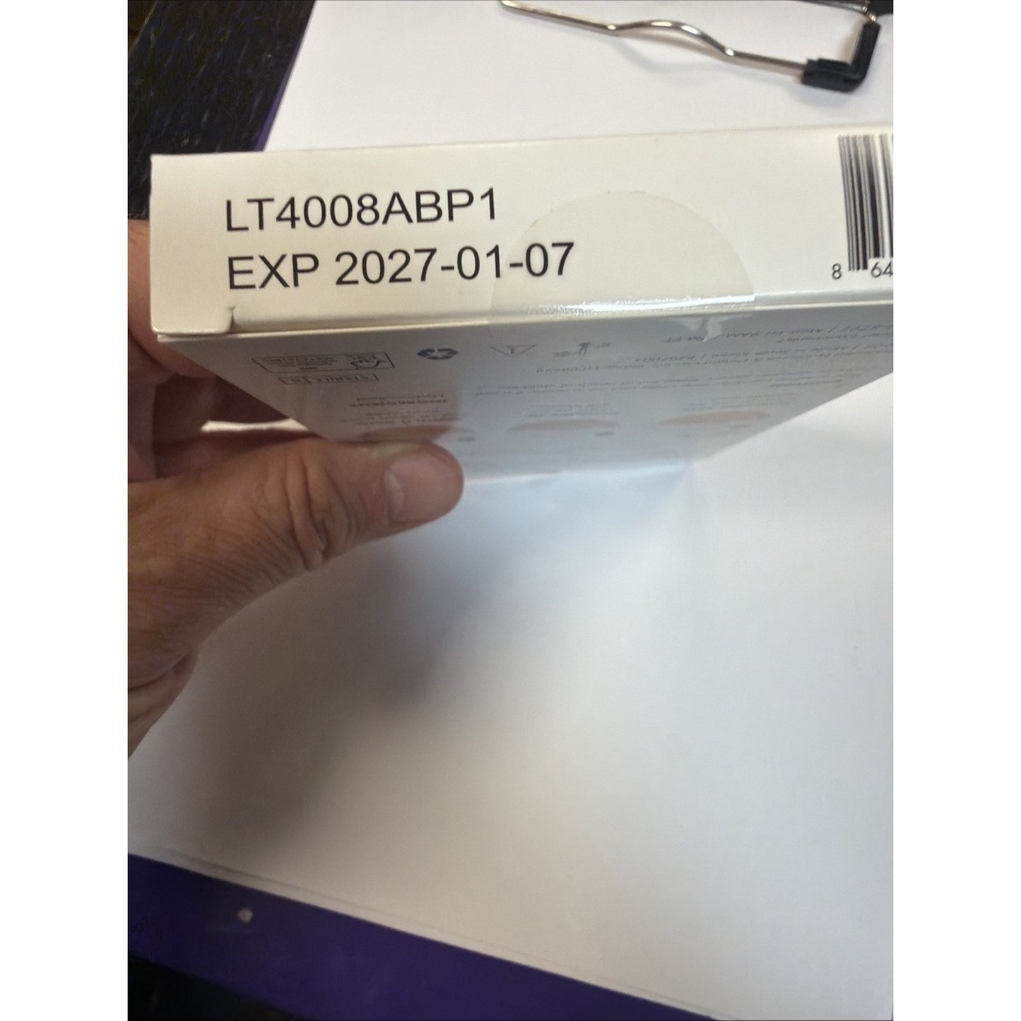 Close-up of a white product box corner held by a hand, showing a printed batch code "LT4008ABP1" and expiration date "EXP 2027-01-07" near a partial barcode.