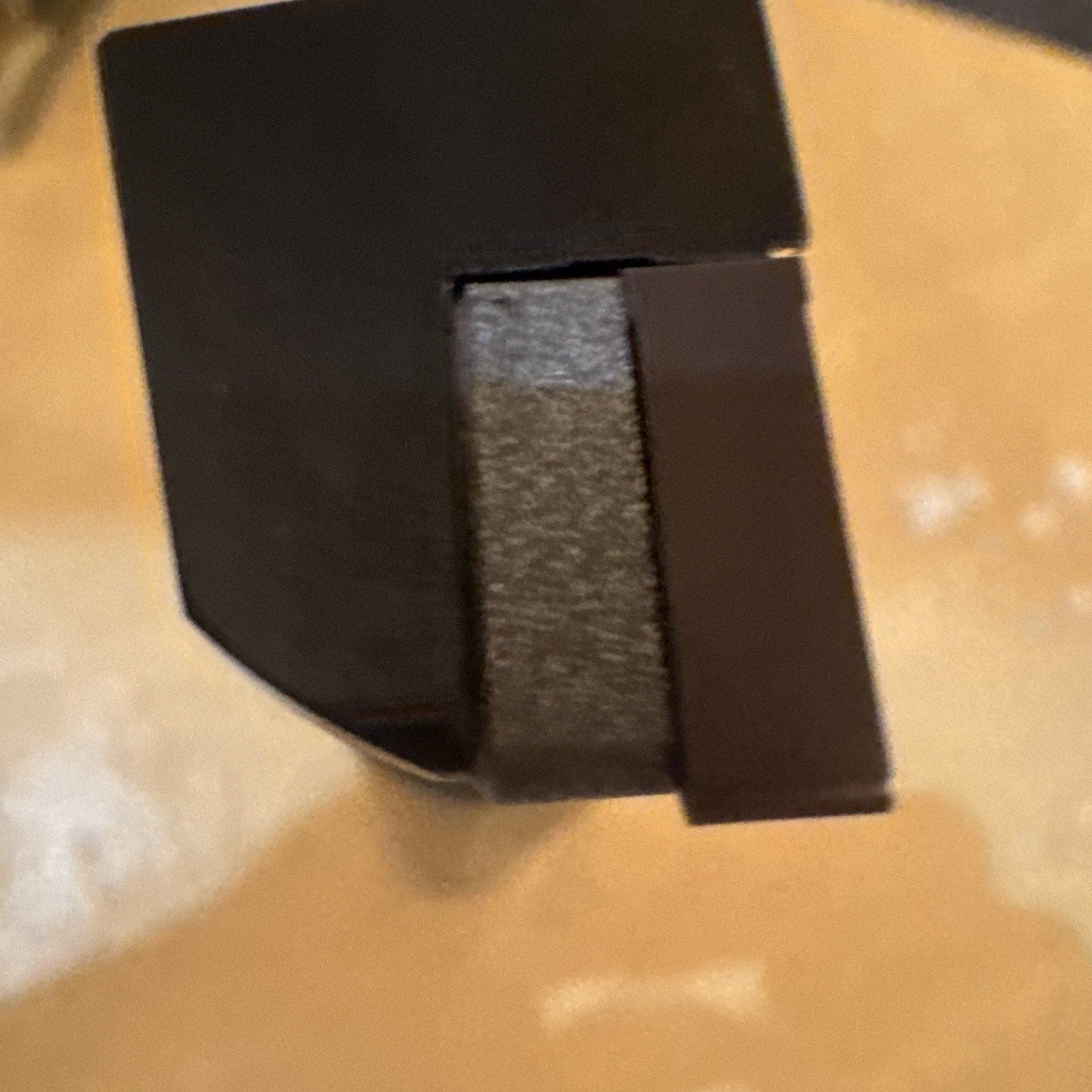 Close-up view of a dark metal tool tip with a flat, rectangular cutting edge extending slightly beyond the body, set against a light beige surface.