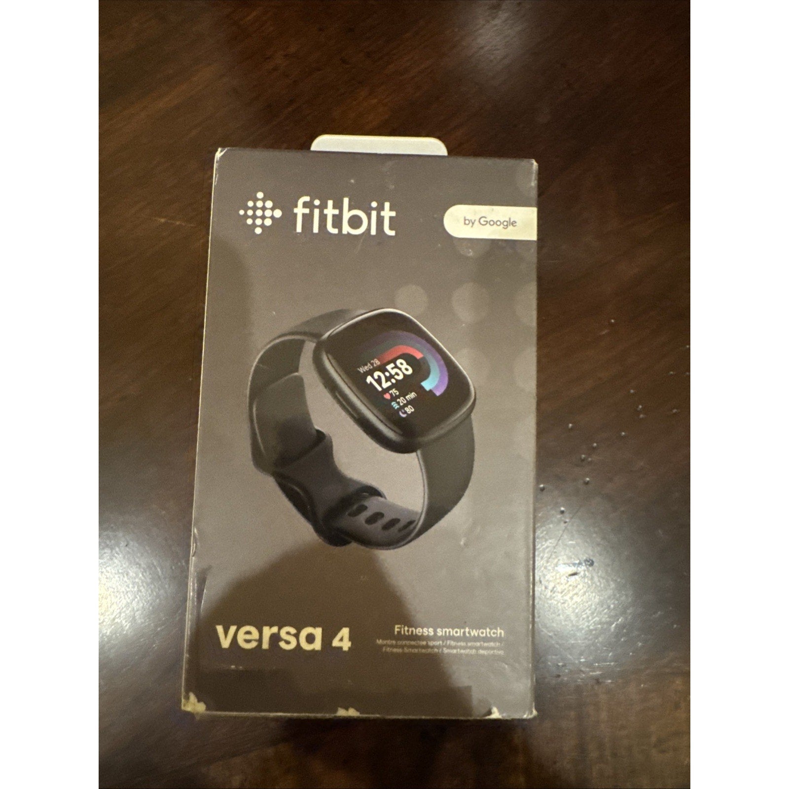 Fitbit Versa 4 fitness smartwatch in black with color display and Google integration on retail packaging box